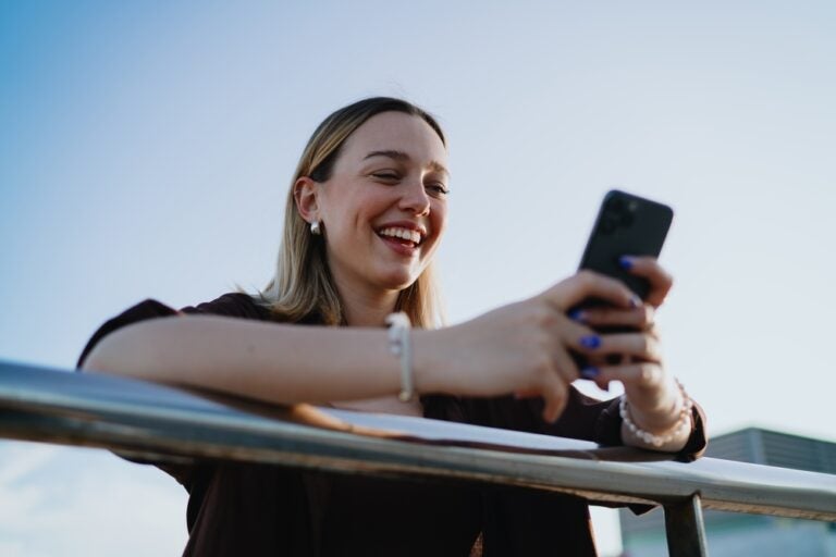 Eine Frau lächelt, während sie auf ihr Handy schaut.