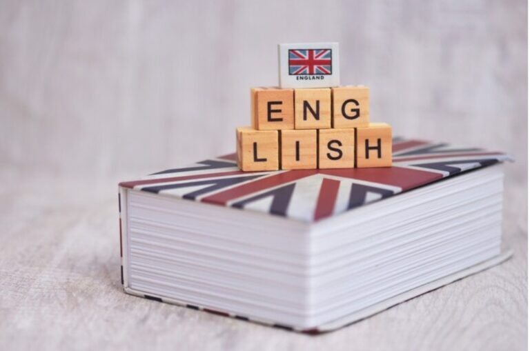 Holzwürfel mit der Aufschrift „ENGLISH“ liegen auf einem Buch mit dem Union-Jack-Design.