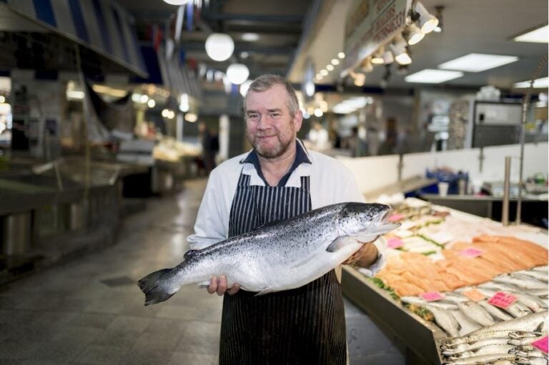 Ein Fischverkäufer präsentiert einen Lachs in einer Markthalle.