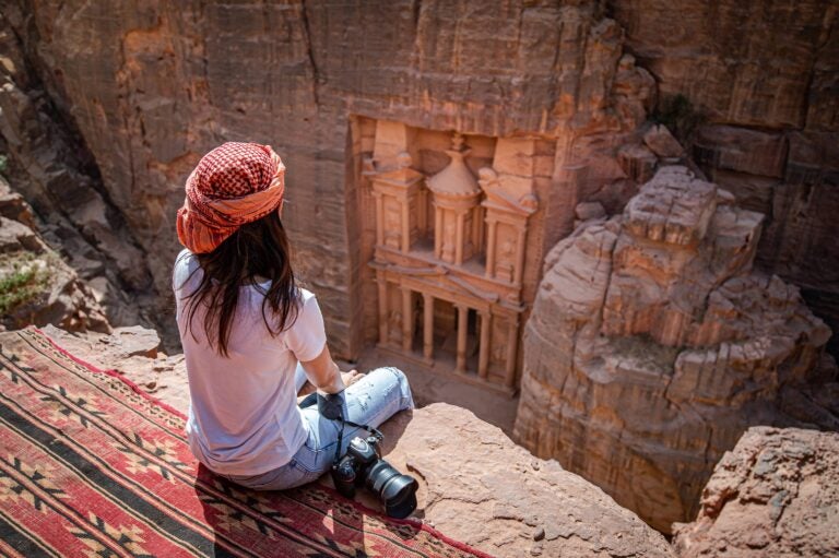 Reisende blickt von einem Felsvorsprung auf das Schatzhaus Al-Khazneh in Petra, Jordanien.
