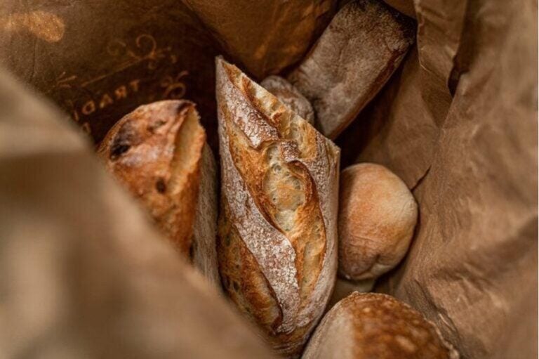 Blick in eine Papiertüte mit mehreren frischen Baguettes und Brötchen