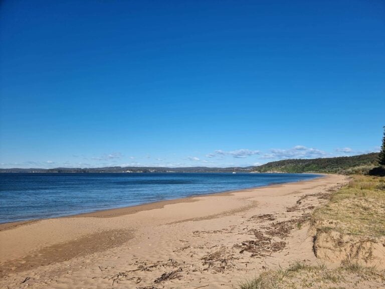Ein weiter, menschenleerer Sandstrand an einer türkisfarbenen Bucht 