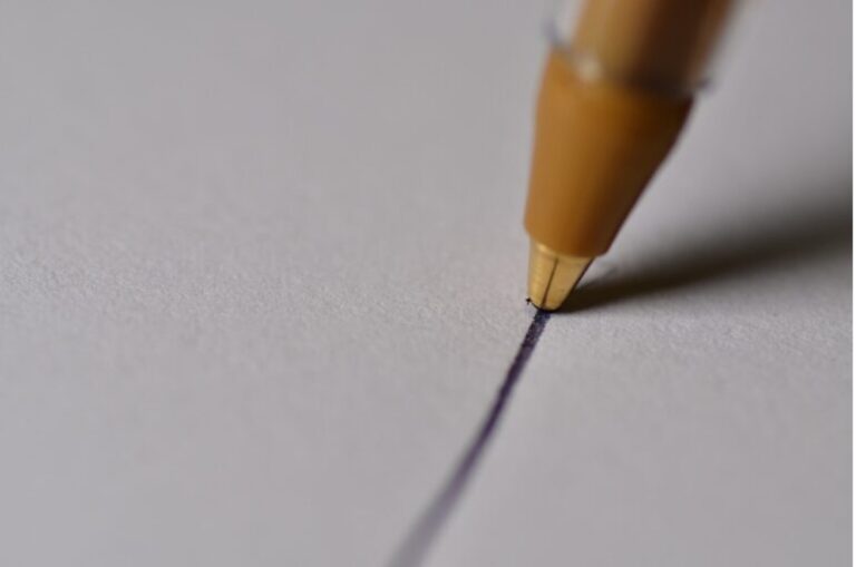 Nahaufnahme einer Kugelschreiberspitze, die eine dunkle Linie auf weißem Papier zieht