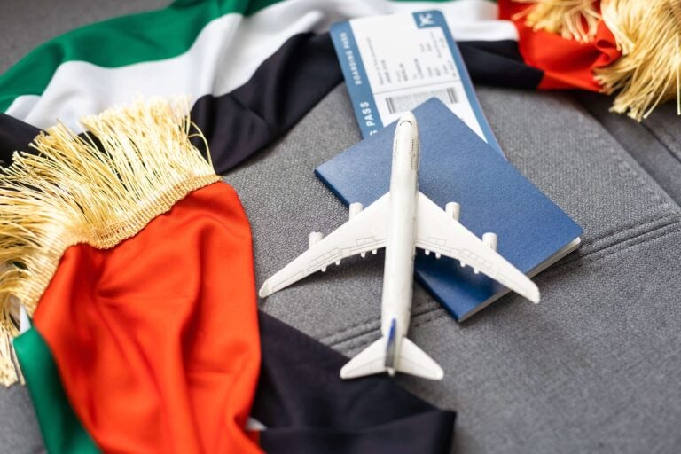 Ein Modellflugzeug liegt auf einem Reisepass und einer Bordkarte, umrahmt von der Nationalflagge der VAE.