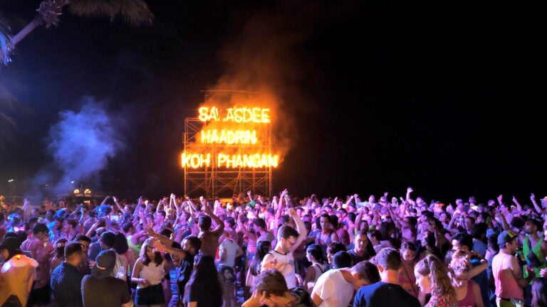 Brennender Schriftzug am Strand über feiernden Menschen bei der Full Moon Party in Thailand.