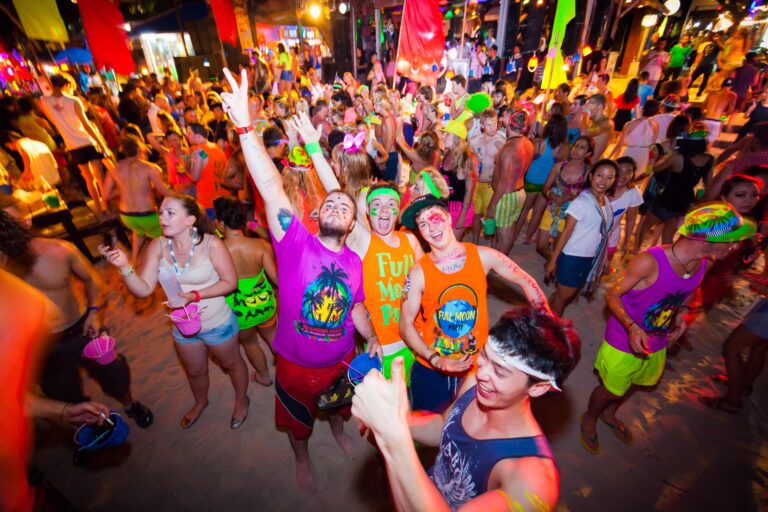Feiernde Menschen in bunten Neon-Outfits am Strand bei der Full Moon Party in Thailand.