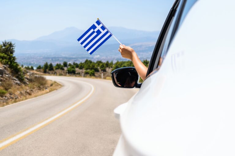 Hand hält eine griechische Flagge aus einem Auto.