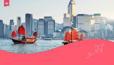 Traditionelle Dschunken mit roten Segeln in der Bucht vor der Skyline von Hongkong