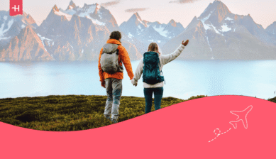 Ein Paar mit Wanderrucksäcken blickt Hand in Hand auf einen Fjord und schneebedeckte Berge