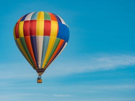 Ein farbenfroh gestreifter Heißluftballon schwebt vor einem klaren, blauen Himmel 