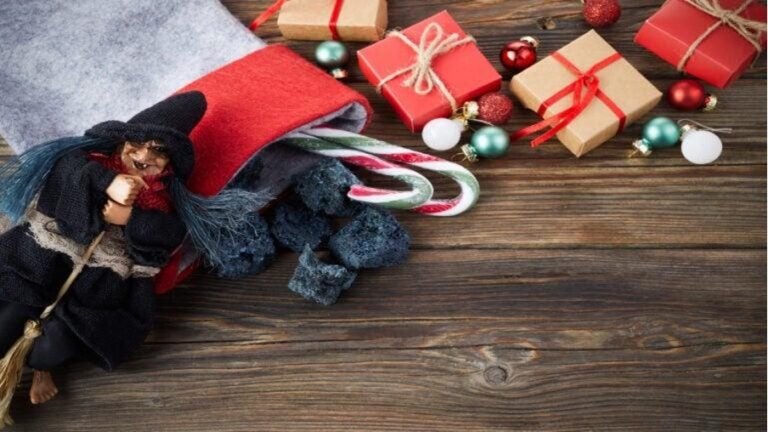 Figur der Hexe Befana neben einem Nikolausstiefel, Süßigkeiten und Geschenken auf einer Holzoberfläche