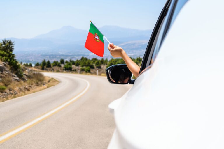 Hand hält eine kleine Flagge Portugals aus einem Autofenster.