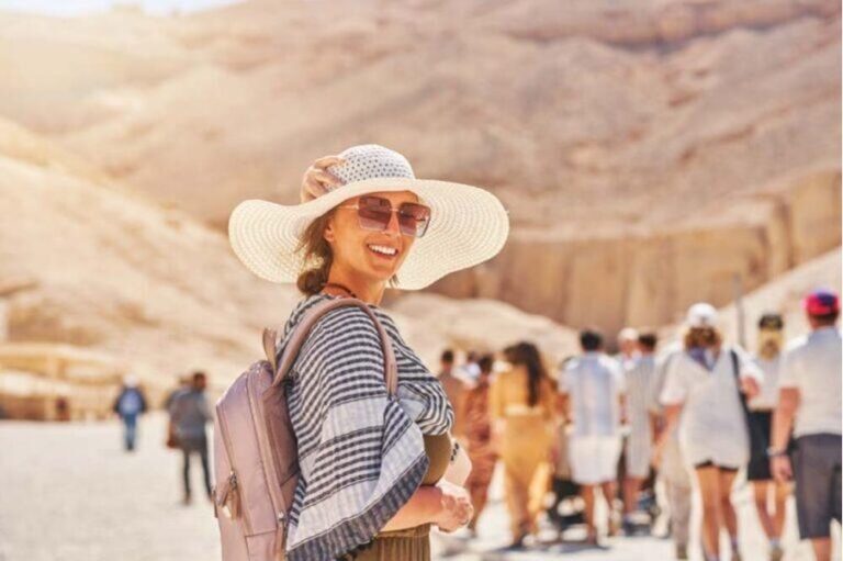 Eine Touristin dreht sich vor einer Reisegruppe in der Wüstenlandschaft eines ägyptischen Tempels um.