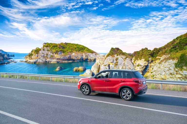 Ein rotes Auto fährt auf einer Küstenstraße in Frankreich vorbei. 