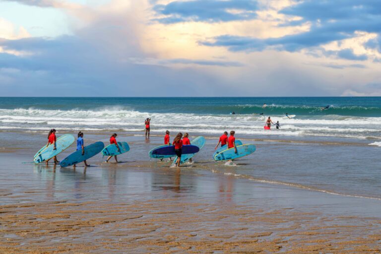 Eine Gruppe von Surfern trägt Surfbretter ins Meerwasser.