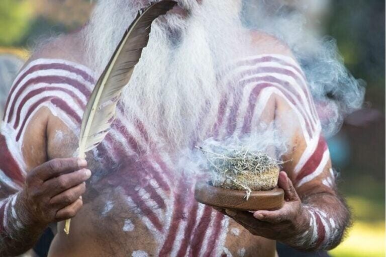 Nahaufnahme eines Aborigines mit traditioneller Körperbemalung während einer Zeremonie mit Feder und Rauch