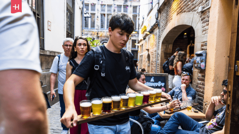 Ein junger Mann trägt ein Holzbrett voller verschiedener Biersorten.