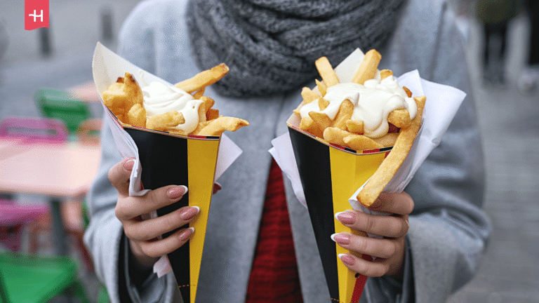 Eine Person hält zwei Papiertüten mit original belgischen Pommes frites.