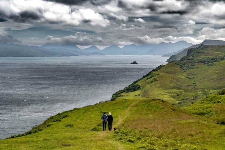 Zwei Personen wandern auf einem grünen Pfad auf der Isle of Skye in Schottland.