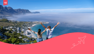 Ein Paar blickt mit ausgestreckten Armen von oben auf Camps Bay in Kapstadt. Passend zum Thema: Ist Kapstadt sicher?