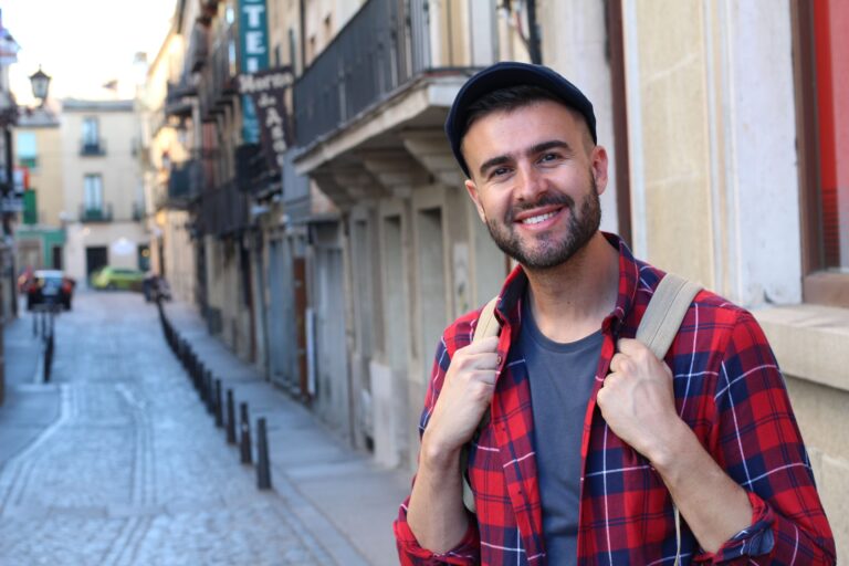 Ein lächelnder Mann mit Rucksack steht in einer europäischen Altstadtgasse.