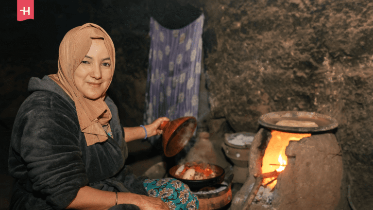 Eine lächelnde Berberfrau öffnet den Deckel einer traditionellen Tajine.