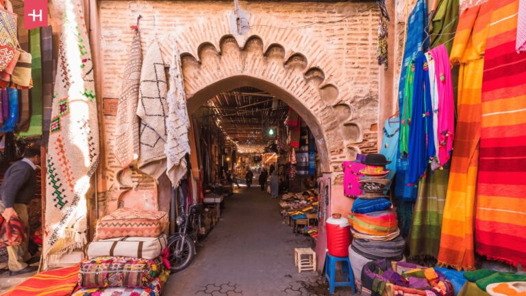Blick durch einen traditionellen Steinbogen in eine schattige Gasse eines Souks in Marrakesch.
