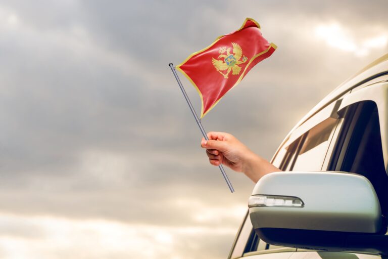 Eine Hand hält die Montenegro-Flagge aus einem Autofenster.