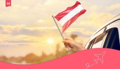 Eine Hand hält die Österreich-Flagge aus dem Autofenster. Passend zum Thema: Österreich Urlaub mit Kindern.