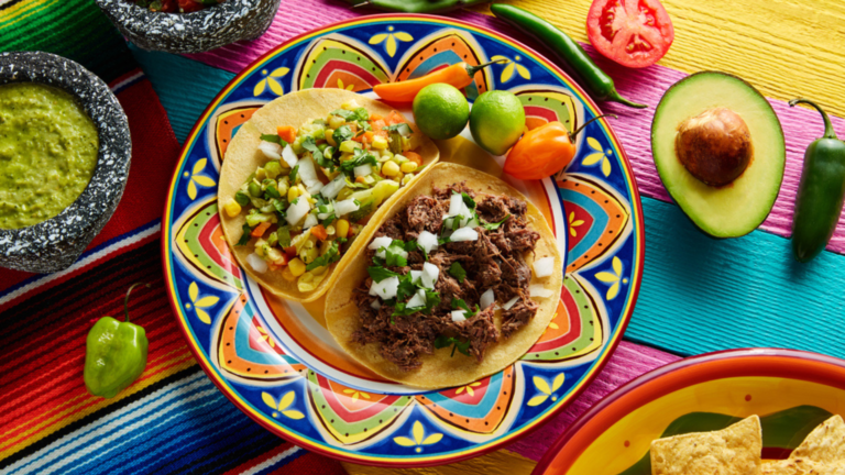 Tacos auf einem Teller auf einem bunt gedeckten Tisch.