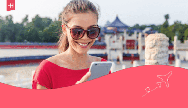 Lächelnde Frau mit Sonnenbrille blickt auf ihr Smartphone.