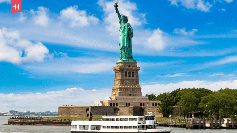 Freiheitsstatue auf Liberty Island mit vorbeifahrender Fähre.