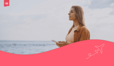 Junge Frau steht mit einem Smartphone am Meer.