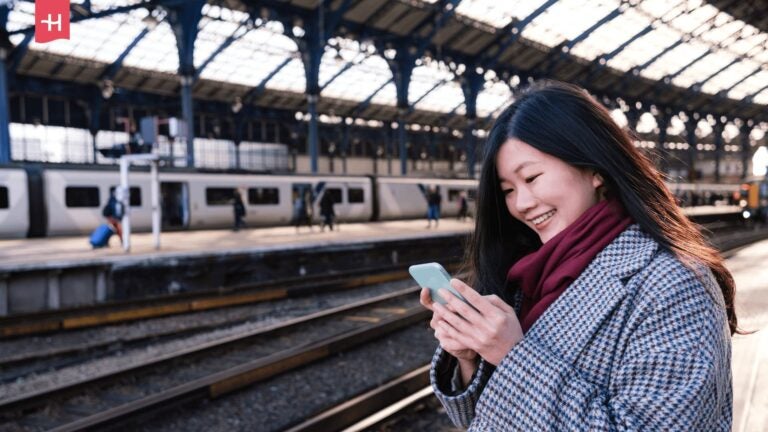 Frau mit Smartphone an einem Bahnhof