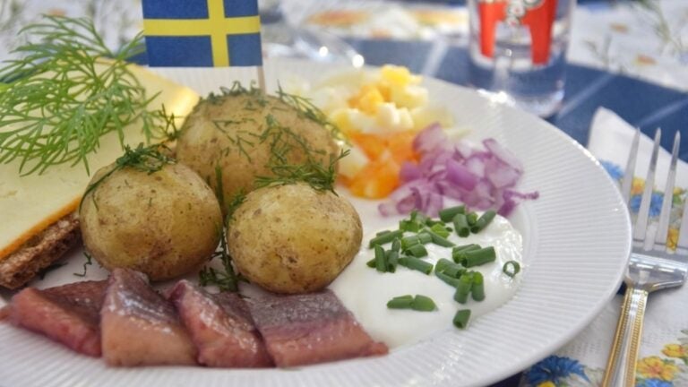 Ein Teller mit Surströmming und Pellkartoffeln auf einem liebevoll gedecktem Tisch.