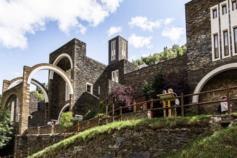 Santuario de Meritxell en Andorra, mostrando la arquitectura de piedra con arcos y ventanas, rodeado de vegetación y montañas.