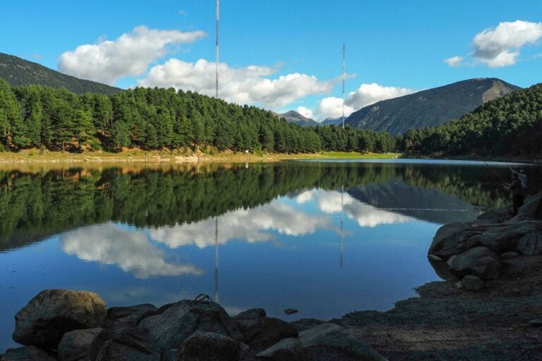 Lago Engolasters en Andorra, con montañas y bosque de pinos reflejados en el agua.