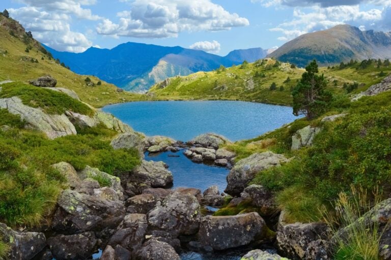 Paisaje del lago de Tristaina en los Pirineos andorranos, con rocas, vegetación y montañas.