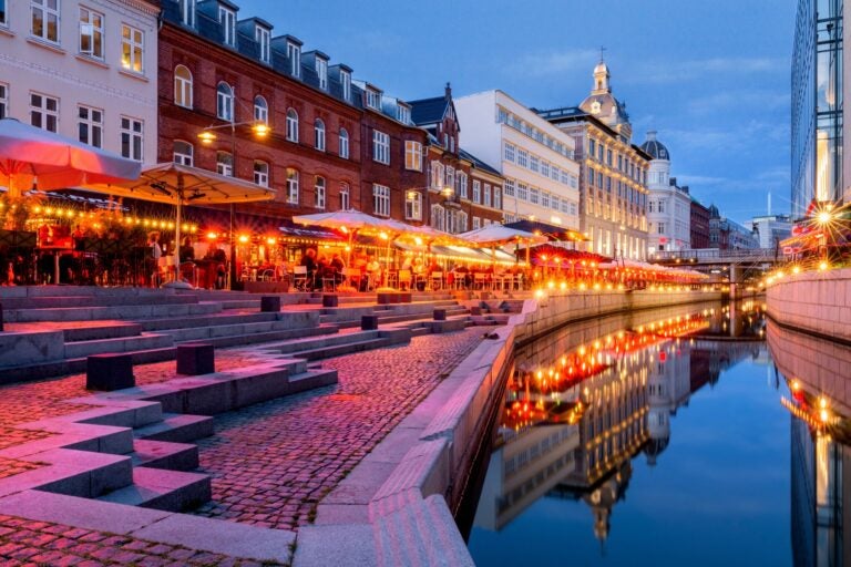 Vista nocturna del canal de Aarhus en Dinamarca, con restaurantes iluminados y reflejos en el agua.