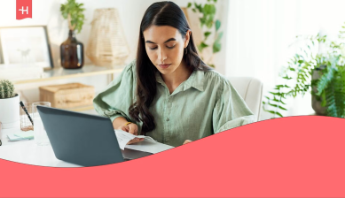 Mujer trabajando con un portátil y revisando documentos en una oficina, imagen del artículo sobre qué es Holafly for Business y cómo funciona.
