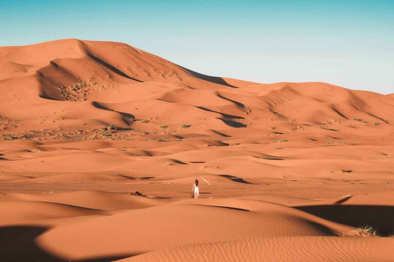 Une jeune femme vêtue de blanc se promenant dans les dunes du désert d'Erg Chegaga au Maroc