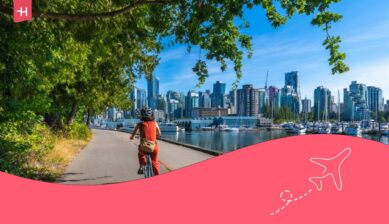 Une femme en promenade à vélo le long de la digue dans le parc Stanley, avec en arrière plant le magnifique paysage urbain de Vancouver, en Colombie-Britannique.
