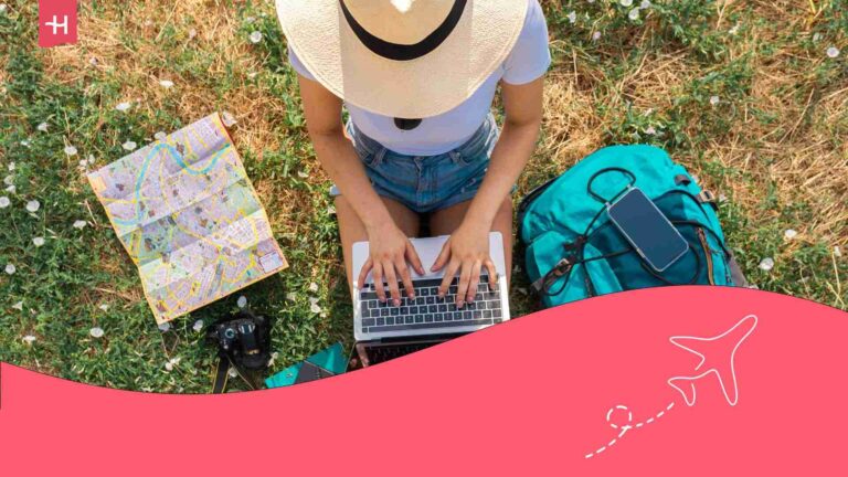 Femme assise dans l'herbe devant son ordinateur en train de préparer son voyage