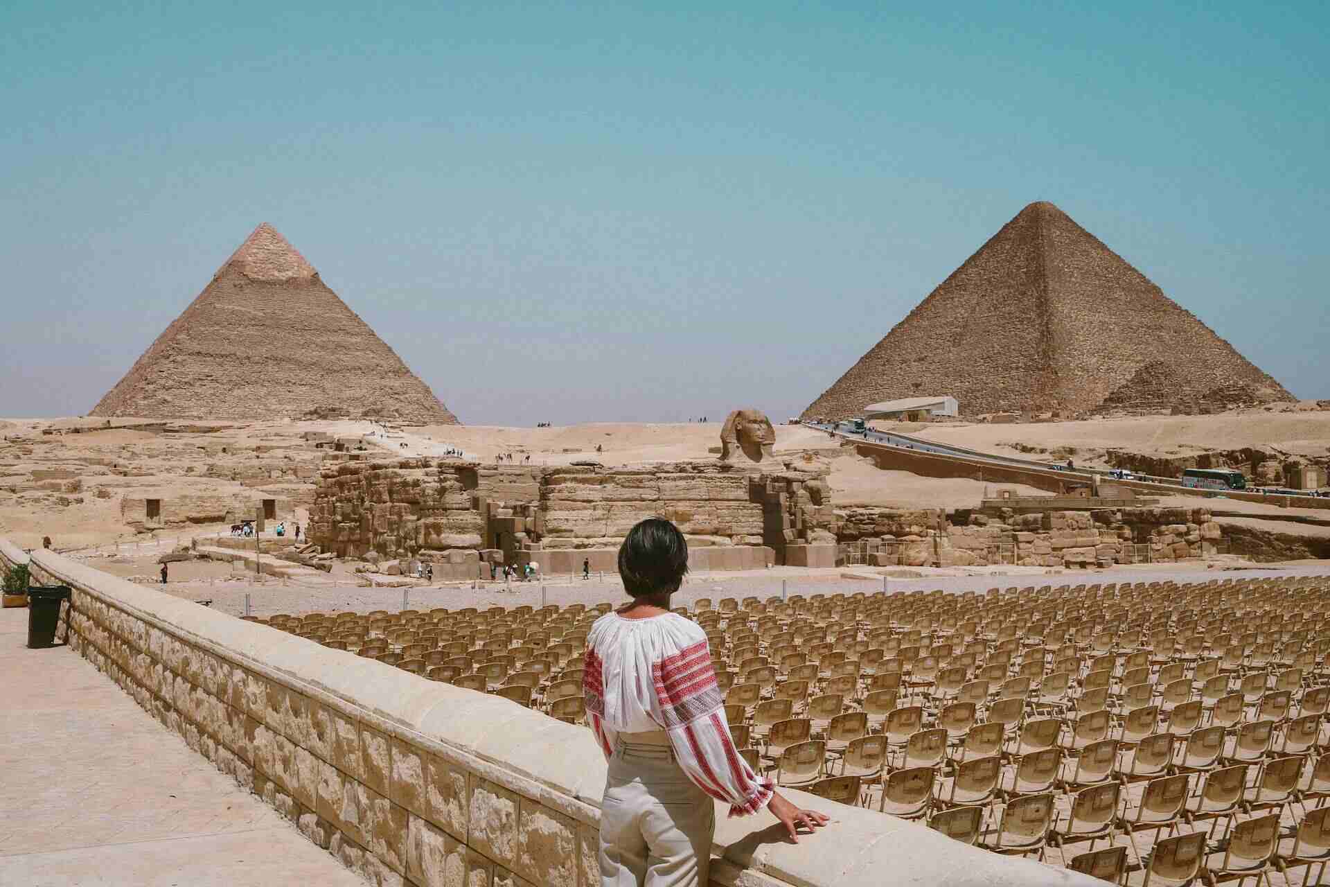 Une femme vue de dos se tenant en face des pyramides en Egypte.