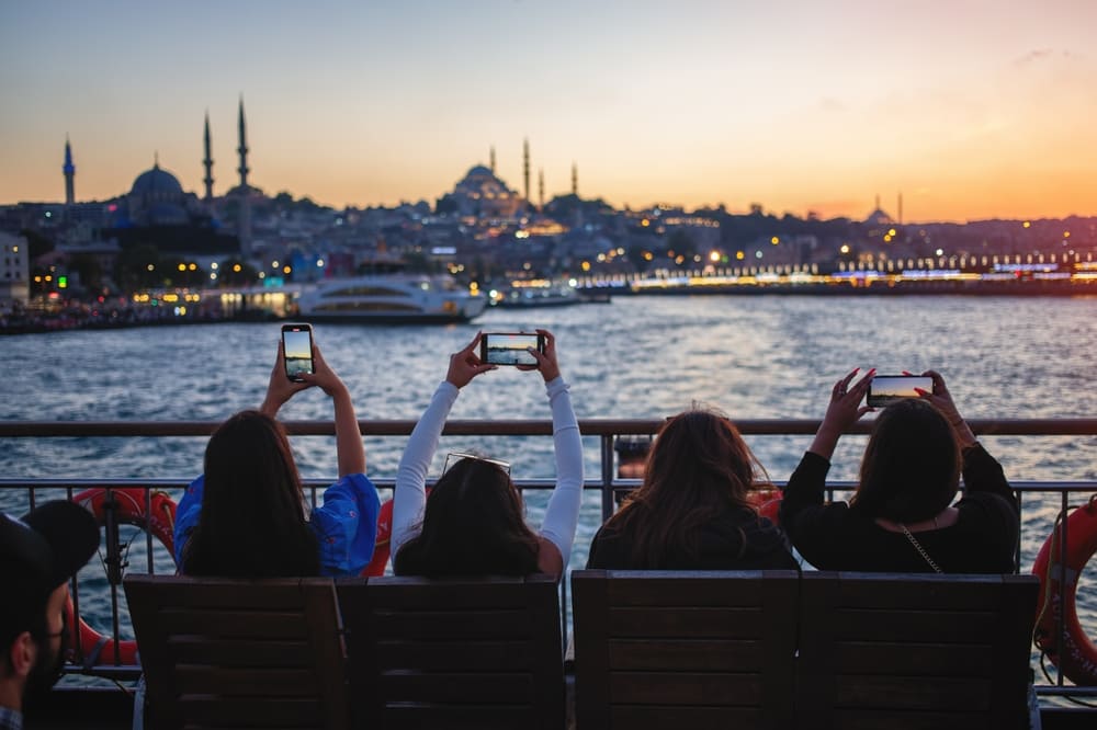 Voyageurs effectuant une traversée en ferry du Bosphore à Istanbul et prenant en photo la ville au coucher du soleil