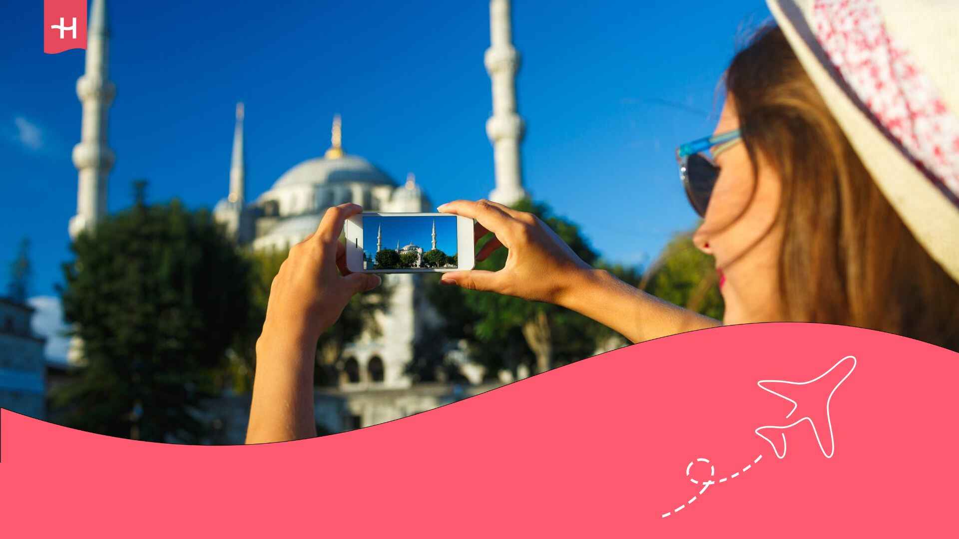 Une jeune femme portant un chapeau en train de prendre une photo de la Mosquée Bleue avec son smartphone