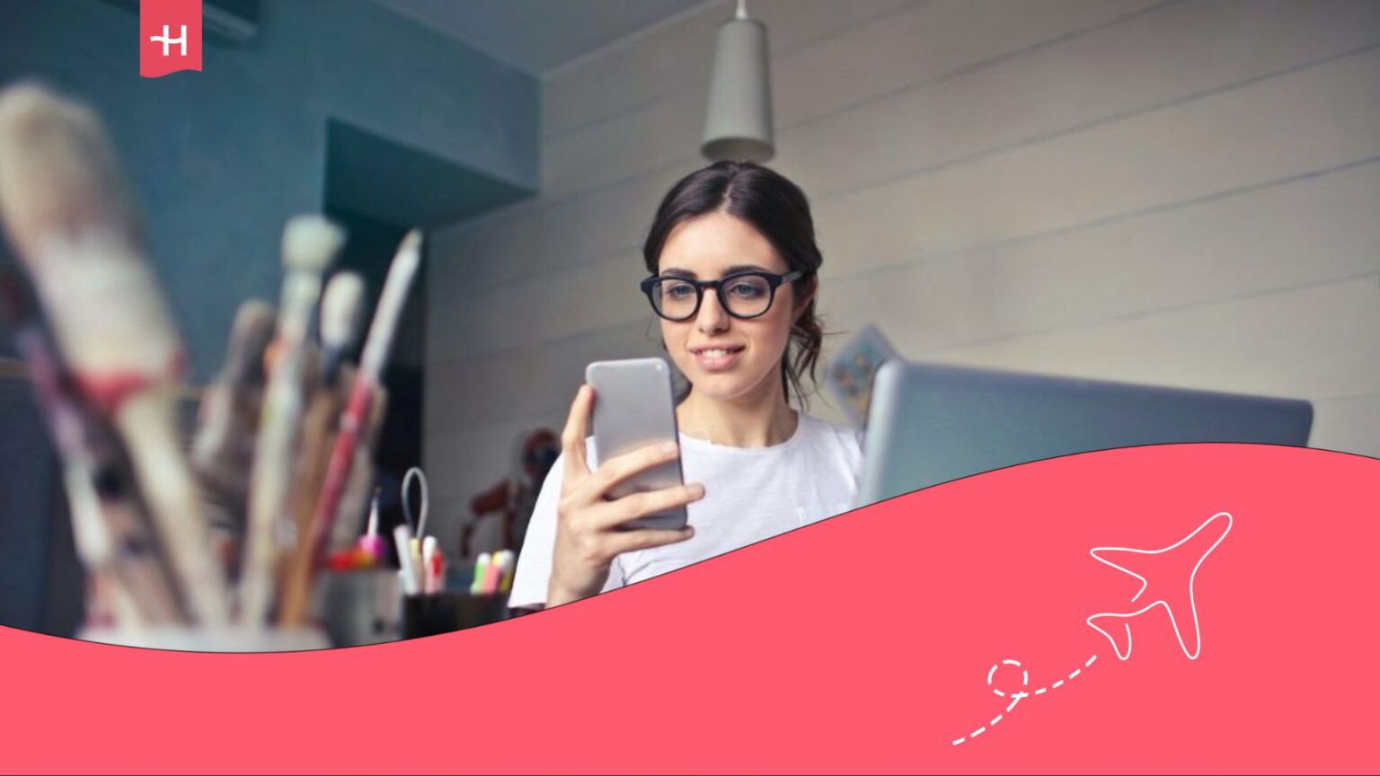 Femme assise à son bureau devant son ordinateur et tenant son smartphone dans la main