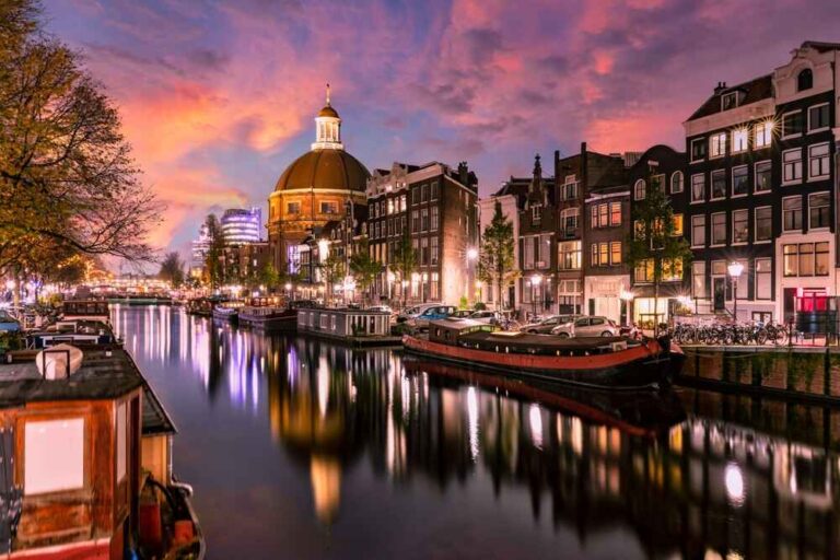 Vue panoramique du canal d'Amsterdam au coucher du soleil avec des bâtiments historiques et des bateaux se reflétant sur l'eau