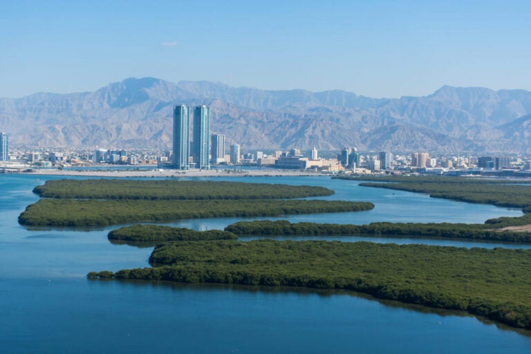 Vue aérienne de Ras el Khaïmah, au nord de Dubaï (Émirats arabes unis), avec un panorama sur la ville, les montagnes du Hajar, le Jebel Jais et les mangroves bordant la Corniche