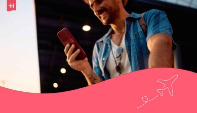 Jeune homme souriant en voyage regardant son GSM et connecté avec le roaming Telenet